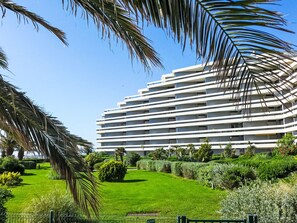 Een modern, meerlaags hotel met een plat dak, omgeven door verzorgde begroeiing en een heldere blauwe lucht.