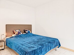 Een bed met een beddekleed met een patroon in blauw, een hoofdbord en twee decoratieve kussens.
