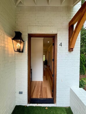 A white brick exterior with a wooden door leading to an interior hallway. - King & Queen-Queen Unit V (Auburn)