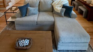 A spacious living room with a sectional sofa, a coffee table, and a dining area with a kitchen in the background.