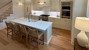 A modern kitchen with a central island, wooden chairs, and pendant lighting.