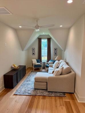 A room with a ceiling fan, a sofa, a chair, a small table, and a window with curtains.