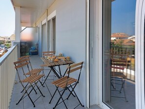 A balcony with a table set for four, equipped with chairs, and a view of buildings in the background. - Les Dunes by Interhome (Mimizan)