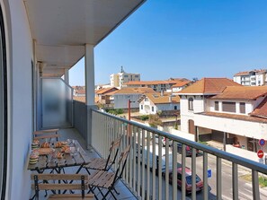 Ein Balkon mit Tisch und Stühlen mit Blick auf ein Wohngebiet mit Gebäuden und parkenden Autos.