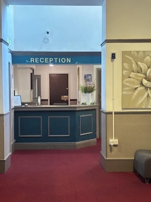 A reception area with a blue counter, a reception desk, a red carpet, and a wall with a large flower painting. - The Midland Hotel & Bar (Mansfield)