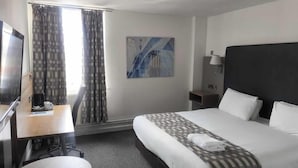 Habitación de hotel con cama, escritorio con silla, televisor y ventana con cortinas.