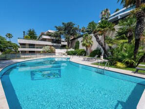Ein Schwimmbad mit Liegestühlen, umgeben von Palmen und einem modernen Gebäude mit Balkonen.