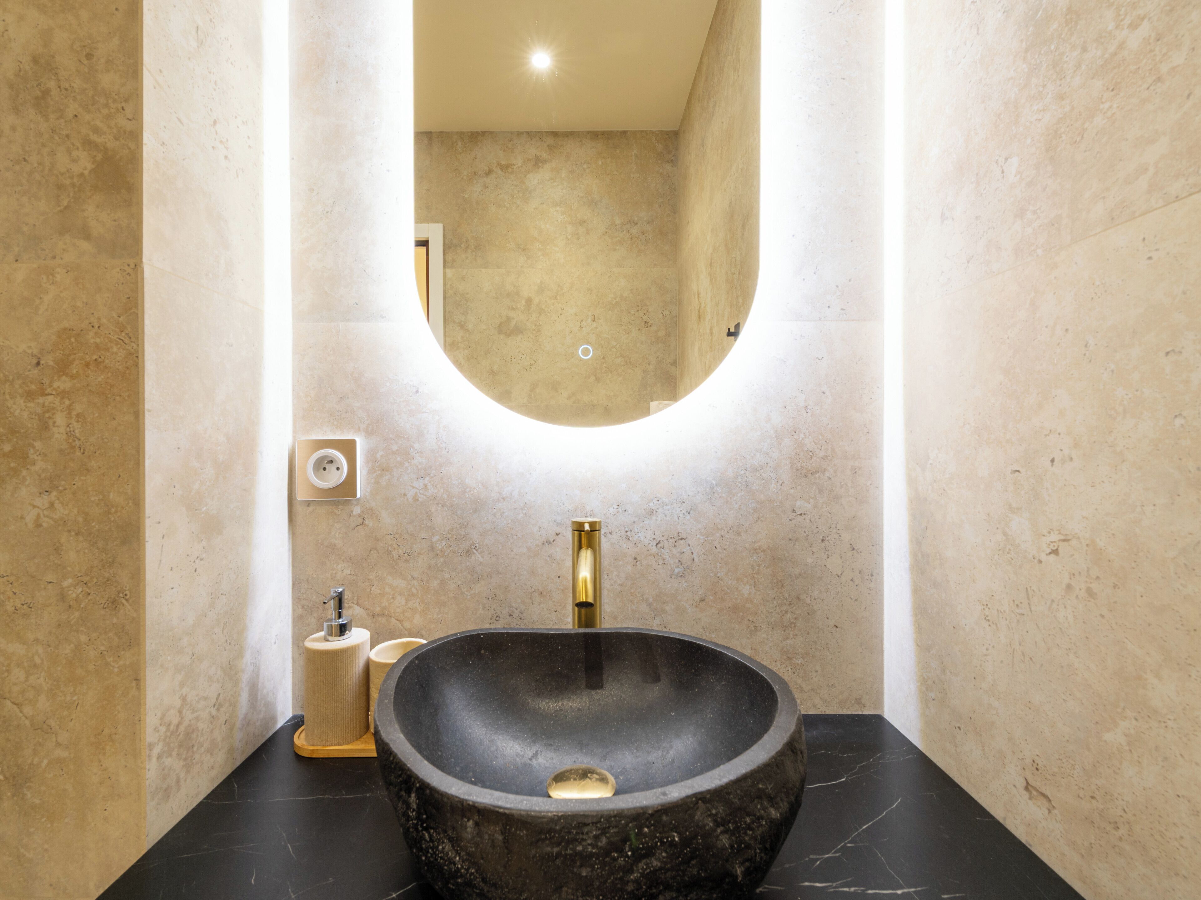 Une salle de bain avec un grand lavabo rond de couleur noire, un robinet doré et un miroir au-dessus du lavabo.