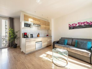Eine moderne Küche mit Holzausstattung, einer Mikrowelle und einer Kaffeemaschine. Es gibt einen Glastisch und eine Couch mit Kissen.