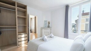 Ett hotellrum med en säng, en garderob, en öppen spis och utsikt över byggnader.