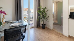 En modern lägenhet med en balkong, en matplats med bord och stolar, en krukväxt och utsikt över stadsbilden.
