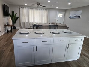 A modern kitchen with white cabinets, a marble countertop, and a dining area with a table set for four.