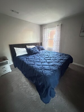 Ein Schlafzimmer mit einem Bett, einem Nachttisch, einem Fenster mit Vorhängen und einer Wandleuchte.