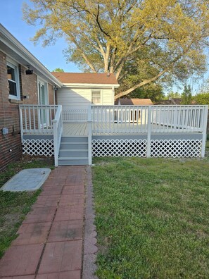 A residential property with a front deck, a brick house, and a large tree.