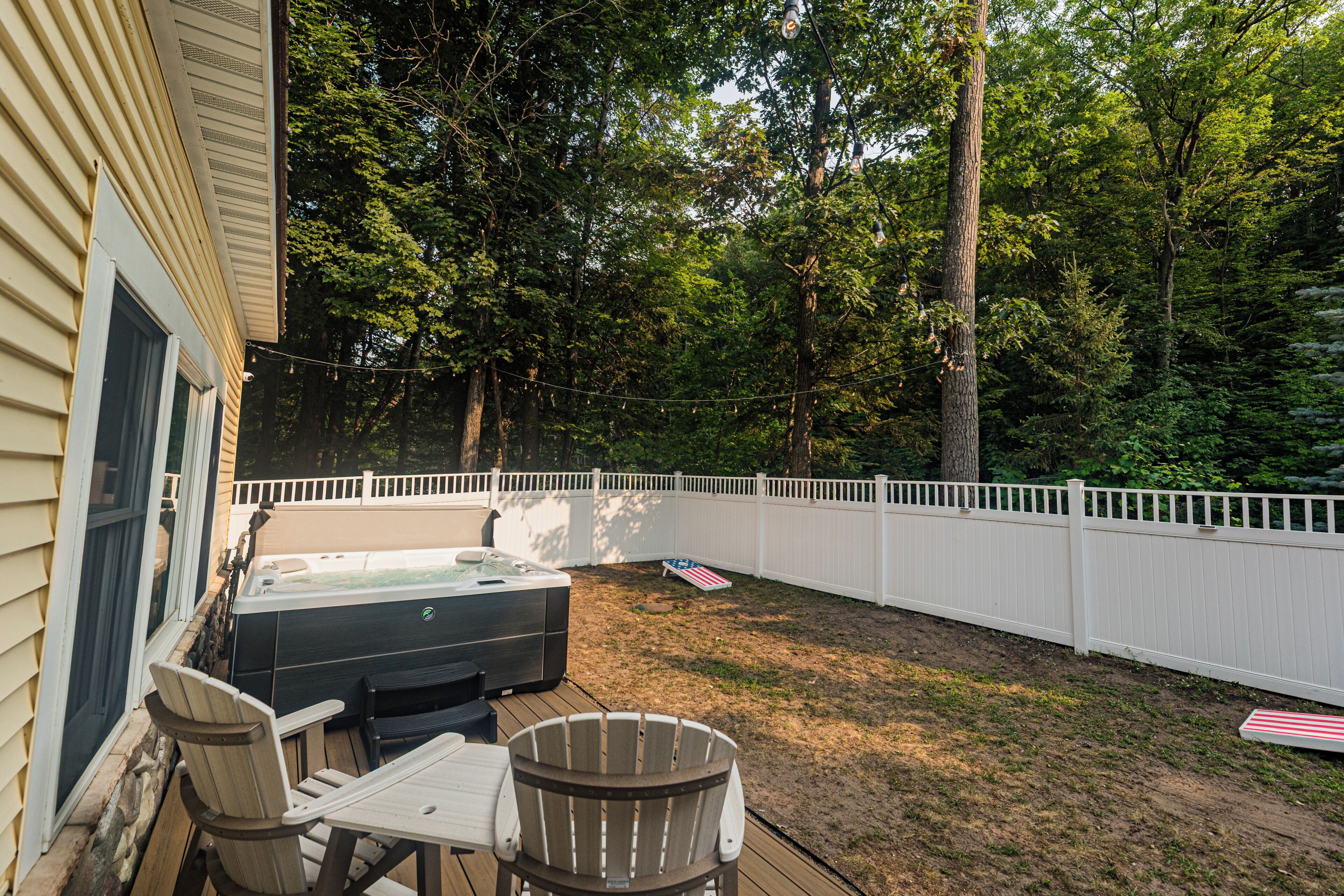 Un jardin avec un jacuzzi, des chaises longues et une clôture blanche.
