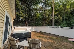 Un jardin avec un jacuzzi, des chaises longues et une clôture blanche.