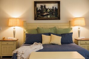 Ein ordentlich bezogenes Bett mit Kopfteil, zwei Nachttischlampen und einem Bild darüber.