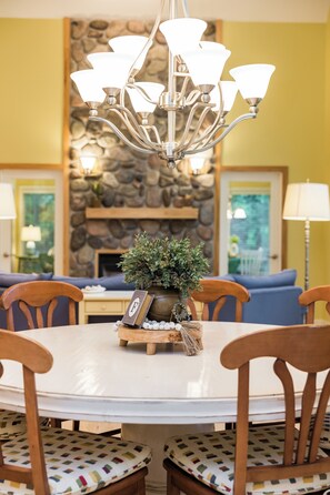 A dining area with a round table, wooden chairs, a chandelier, a potted plant, and a stone wall in the background. - Hot Tub-Game Room-Sun Room-Backyard-King-7 TVs-5 Bedrooms-4300 SqFt. Sleeps 12 (Honor)