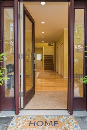 Une porte en bois avec des panneaux de verre, donnant sur un couloir dont l’entrée est agrémentée d’un paillasson.