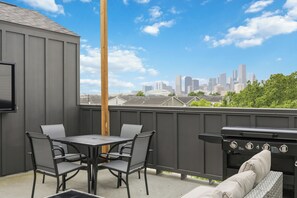 A rooftop patio with a grill, dining table, and chairs, overlooking a city skyline. - Wabi Sabi Sanctuary Rooftop in EADO (Houston)