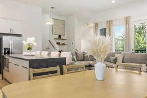 A modern kitchen with a central island, dining table, and chairs. There is a sofa and a window with curtains. - Wabi Sabi Sanctuary Rooftop in EADO (Houston)