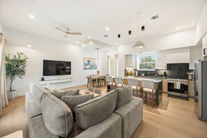 A modern living room with a sofa, TV, dining area, and kitchen. - Wabi Sabi Sanctuary Rooftop in EADO (Houston)