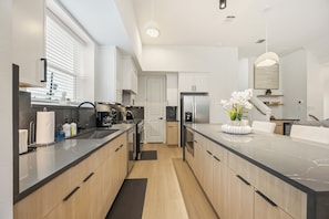 A modern kitchen with a marble countertop, wooden cabinets, a stainless steel refrigerator, and a potted orchid on the island. - Wabi Sabi Sanctuary Rooftop in EADO (Houston)