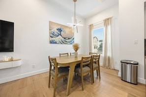 A dining area with a wooden table and chairs, a painting on the wall, a ceiling light fixture, and a window with curtains. - Wabi Sabi Sanctuary Rooftop in EADO (Houston)