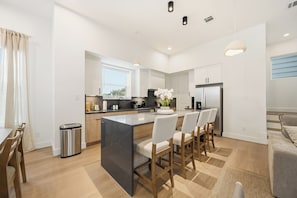 A modern kitchen with a central island, white cabinetry, and a dining area with chairs. - Wabi Sabi Sanctuary Rooftop in EADO (Houston)