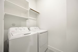 A laundry room with two white washing machines and a shelf above. - Wabi Sabi Sanctuary Rooftop in EADO (Houston)