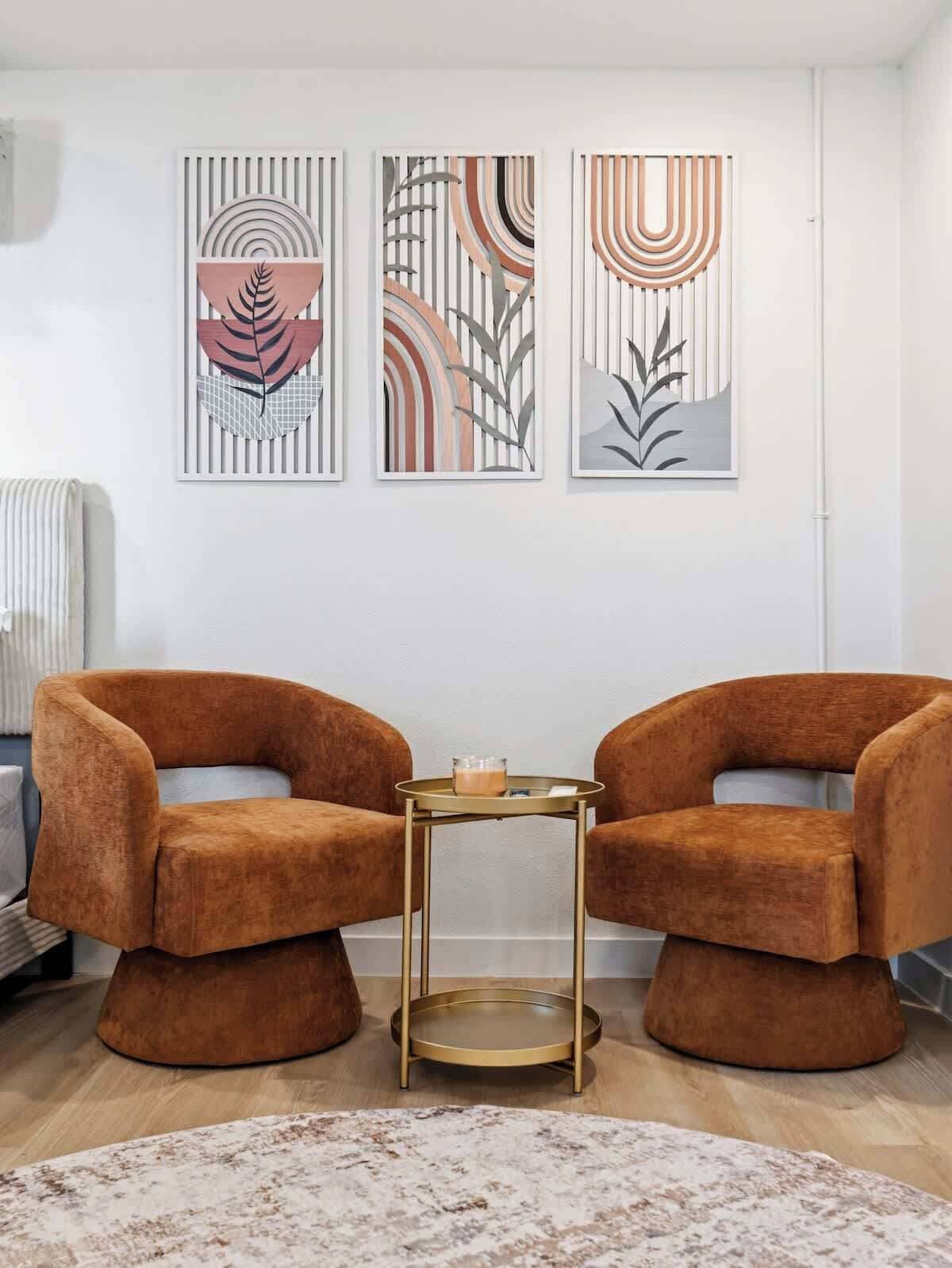 A modern living room with two brown velvet armchairs, a small round table with a candle, and abstract wall art.