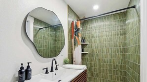 Een badkamer met een ronde spiegel, een witte wastafel en een douchecel met gordijn.