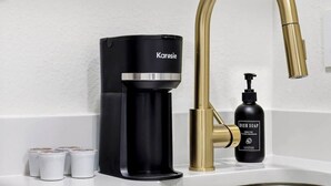 Een moderne keuken met een zwarte koffiezetapparaat, een gouden kraan en een fles afwasmiddel.
