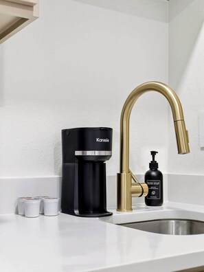 Eine moderne Küche mit einer schwarzen Kaffeemaschine, einem goldenen Wasserhahn und einer Flasche Spülmittel.