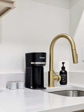 A modern kitchen with a black coffee maker, a gold faucet, and a dish soap bottle. - Stylish Cozy Studio in Bishop Arts Prime Walkable Location #6 (Dallas)