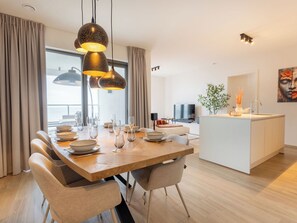 A modern dining area with a wooden table, chairs, and pendant lighting. - O'Sea with seaview & terrace by Interhome (Oostende)