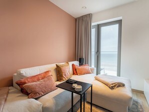 A modern hotel room with a sofa, a small table, a remote control, and a view of the ocean through a large window. - O'Sea with seaview & terrace by Interhome (Oostende)