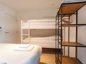 Ein Etagenbett mit einer Holzleiter, eine weiße Tür mit Schloss und ein Bett mit weißer Decke.