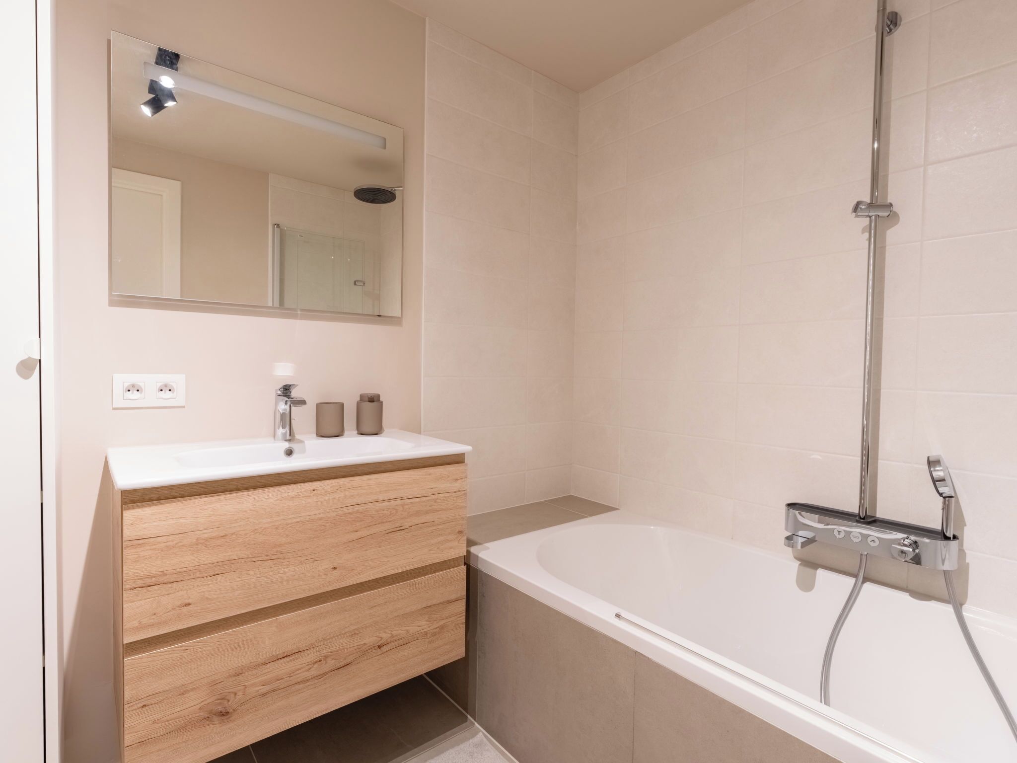 Un baño con lavamanos blanco, tocador de madera, espejo y bañera con ducha.