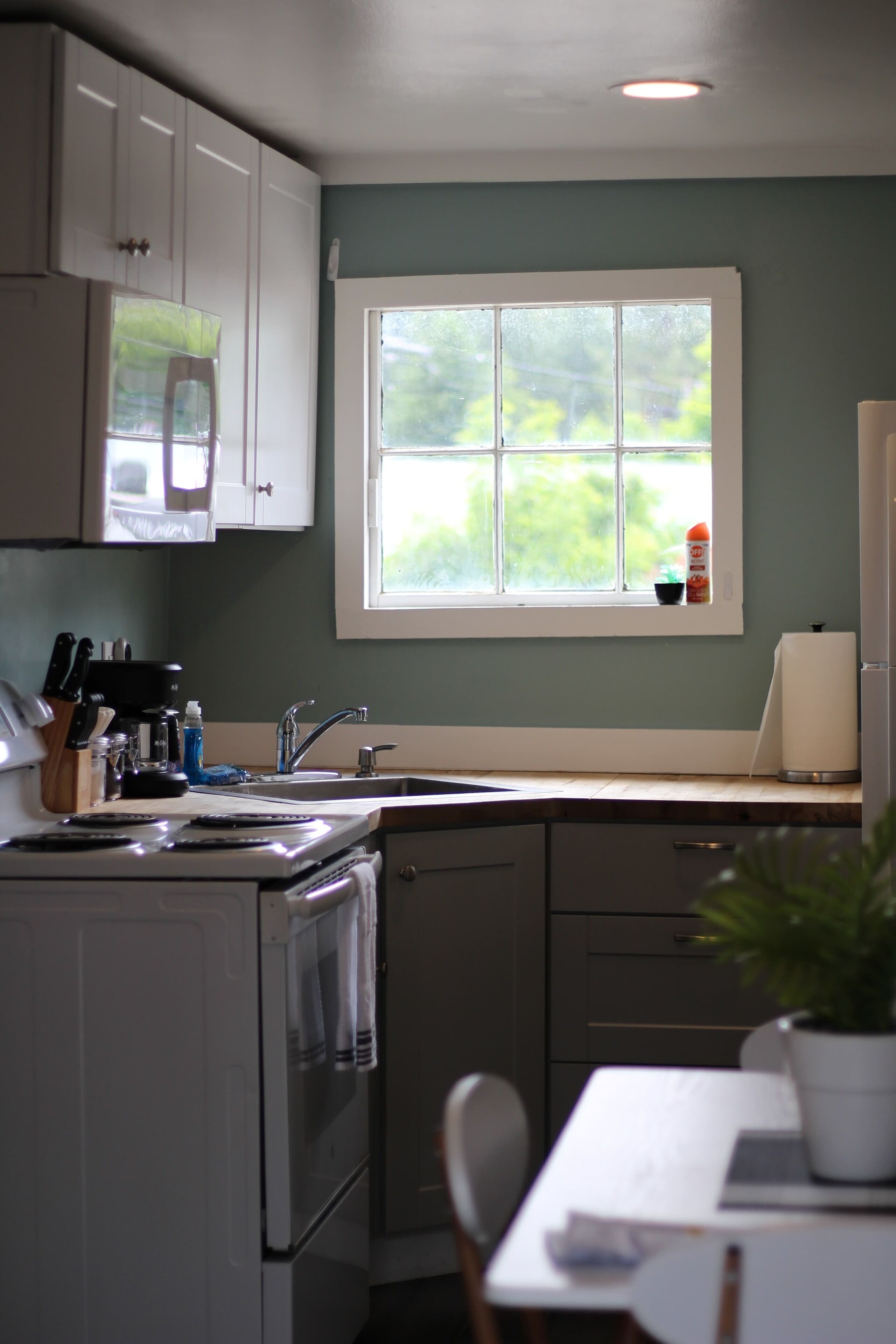 A kitchen with white cabinets, a stove, a sink, and a window with a view of greenery.