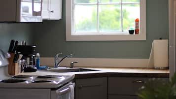 A kitchen with white cabinets, a stove, a sink, and a window with a view of greenery.