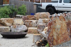 A paved outdoor area with large rocks, a metal fire pit, and a wooden stump. - Shore Acres -Cabin 2 Lakeview (Loon Lake)