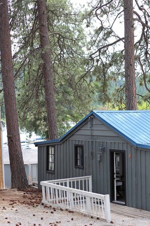 A small cabin with a metal roof, a white porch, and a door leading to the interior.