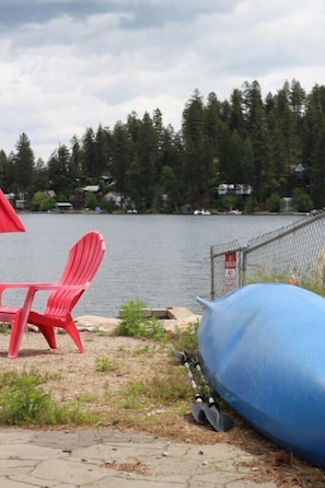 A lakeside view with a red chair, a blue barrel, and a chain-link fence. - Shore Acres -Cabin 2 Lakeview (Loon Lake)
