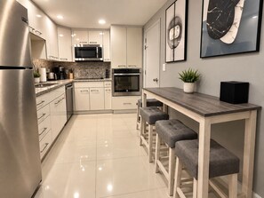 Eine moderne Küche mit Edelstahlgeräten, einer Marmor-Spritzschutzwand und einem Holzespeisetisch mit Barhocker.