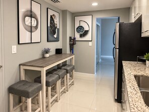 Eine moderne Küche mit einem eingebauten Kühlschrank, einer Holzelemente-Bar mit gepolsterten Hocker und abstrakter Wandkunst.