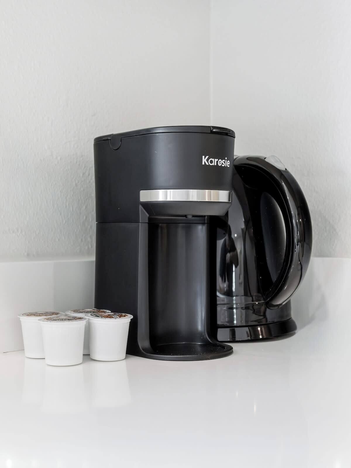 A black coffee maker with a glass carafe and two white disposable cups on a white countertop.