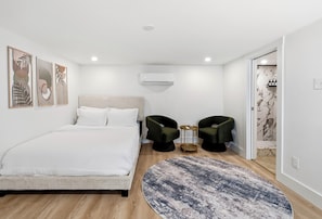 Ein modernes Schlafzimmer mit einem Bett, zwei Sesseln, einem runden Teppich und Wandbildern.