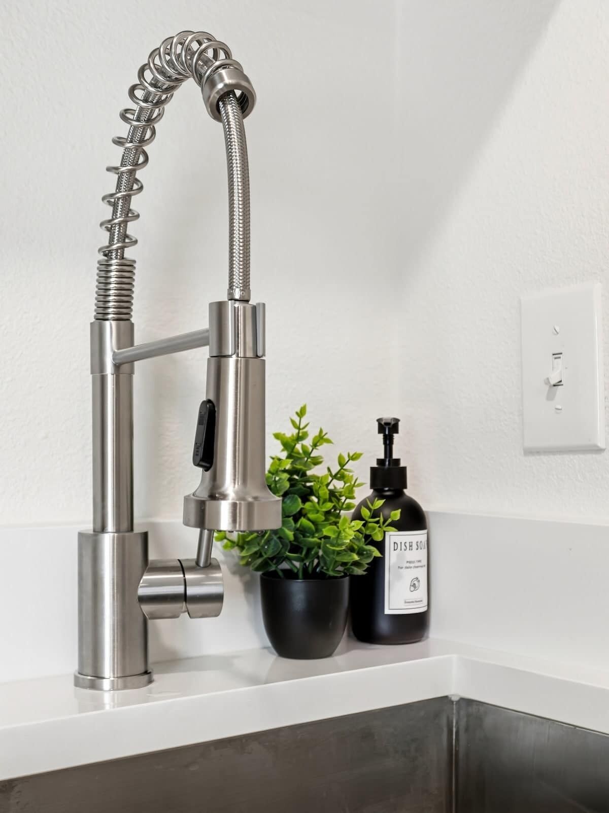 A modern kitchen faucet with a flexible hose, a potted plant, and a black bottle with a pump.