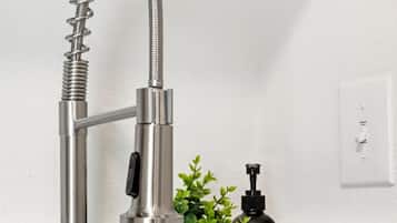 A modern kitchen faucet with a flexible hose, a potted plant, and a black bottle with a pump.